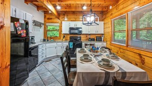 A wooden cabin kitchen with white cabinets, a black refrigerator, a microwave, and a dining table set for four. - Location! Hot Tub, Game Room, Playground, 2K+ Sq Feet, Easy Roads! (Gatlinburg)