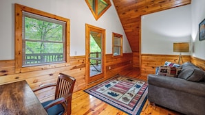 A cozy cabin interior with wooden walls, a dining area with a table and chairs, a sofa, and a patterned rug. - Location! Hot Tub, Game Room, Playground, 2K+ Sq Feet, Easy Roads! (Gatlinburg)