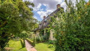 A traditional house with a thatched roof, surrounded by lush greenery and a paved pathway leading to the entrance. - The Granary, Dunstall Green (Newmarket)