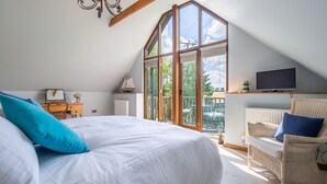 A bedroom with a large bed, a television, a wicker chair, and a view of the outdoors. - The Granary, Dunstall Green (Newmarket)