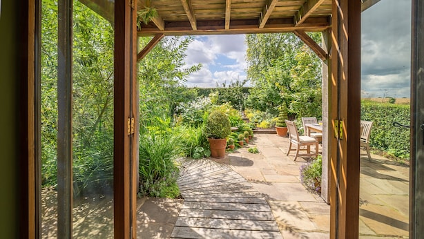 An open wooden structure leading to a garden patio with potted plants and outdoor furniture. - The Granary, Dunstall Green (Newmarket)
