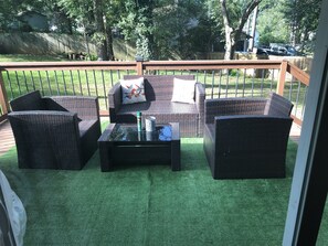 Eine überdachte Terrasse mit Korbmöbeln, einem Glastisch und Blick auf den Garten.