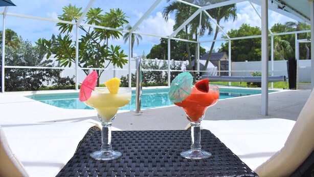 Deux verres à cocktail sont posés sur une table près d’une piscine, offrant une vue dégagée sur la piscine et les palmiers en arrière-plan.