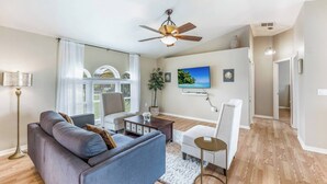 Un salon moderne avec un canapé gris, un fauteuil blanc, une petite table ronde et un ventilateur de plafond.