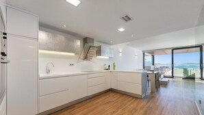 Une cuisine moderne avec des meubles blancs, un plancher en bois et une vue sur la mer grâce à de grandes fenêtres.