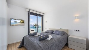 Une chambre moderne avec un grand lit, une table de chevet, un téléviseur fixé au mur et une fenêtre offrant une vue panoramique.