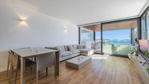 Un salon moderne avec un canapé, une table à manger et une table basse. Une grande fenêtre offre une vue sur la mer.