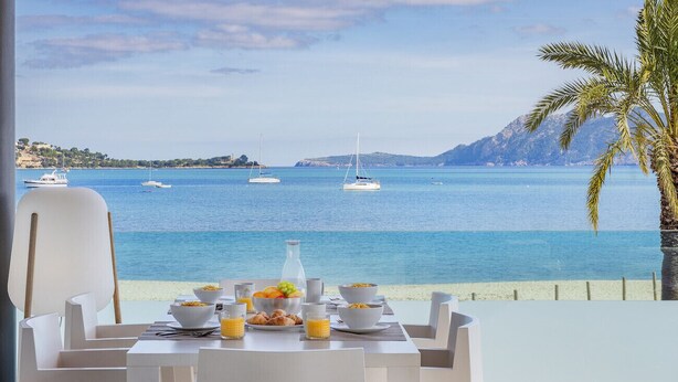 Une table à manger dressée pour le petit-déjeuner, avec vue sur la mer et les bateaux.