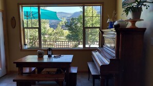 A room with a large window offering a view of a forested area and mountains. There is a wooden table with a bench, a potted plant, and a decorative vase on a stand. - Spacious, custom home, large fenced yard. Fast fiber internet! STR-1-2024-057 (RIDGWAY)