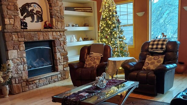 A cozy living room with a stone fireplace, leather armchairs, a glass coffee table, and a Christmas tree. - Spacious, custom home, large fenced yard. Fast fiber internet! STR-1-2024-057 (RIDGWAY)