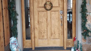 A wooden double door with a wreath, surrounded by evergreen garlands and pine cones, and a 'Merry Christmas' doormat. - Spacious, custom home, large fenced yard. Fast fiber internet! STR-1-2024-057 (RIDGWAY)