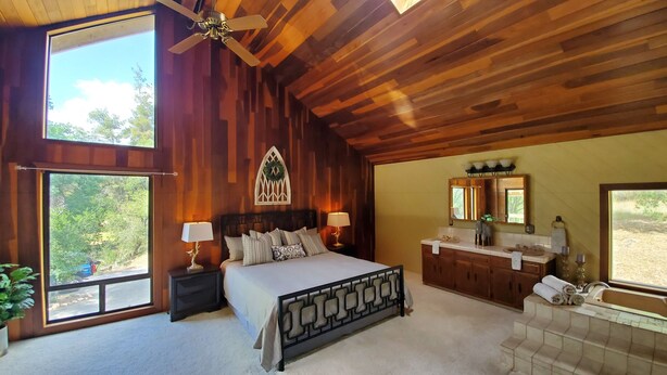 A bedroom with a large bed, a wooden ceiling, a window, a nightstand, a dresser, and a mirror. - Private house close to Sequoia National Park with pool and private river access (Three Rivers)