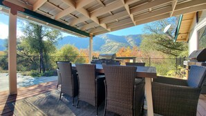 An outdoor patio with a grill, wicker chairs, and a view of mountains. - Private house close to Sequoia National Park with pool and private river access (Three Rivers)