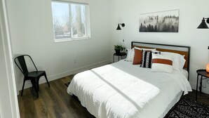 Une chambre à coucher avec un lit, un ventilateur de plafond, une fenêtre, une chaise, une table de chevet, une lampe et un tableau encadré au mur.