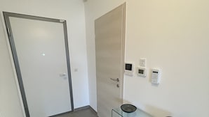 Käytävässä on lasinen konsolipöytä, ovi ja seinälle asennettu termostaatti.