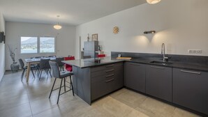 Moderni keittiö, jossa on tummat kaapistot, keskellä oleva keittiösaareke ja riippuvalaisimet.