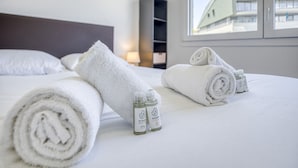 Siististi pedattu sänky, jossa on rullalle taitetut valkoiset pyyhkeet ja kaksi pulloa shampoota.