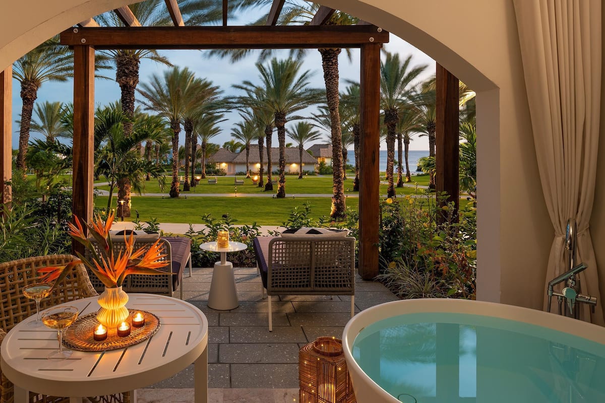 Ein gemütlicher Außenbereich mit Tisch, Stühlen und Whirlpool, mit Blick auf einen gepflegten Garten und einen Pool.