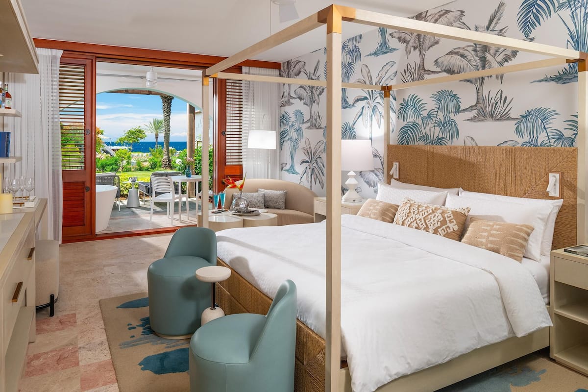 Ein geräumiges Schlafzimmer mit Himmelbett, Balkon mit Meerblick und tropisch gestalteter Tapete.