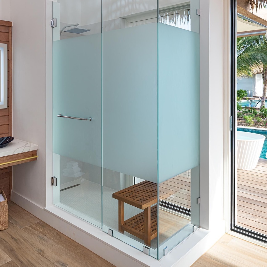 A modern bathroom with a glass-enclosed shower, a wooden vanity with a large mirror, and a view of a pool outside.