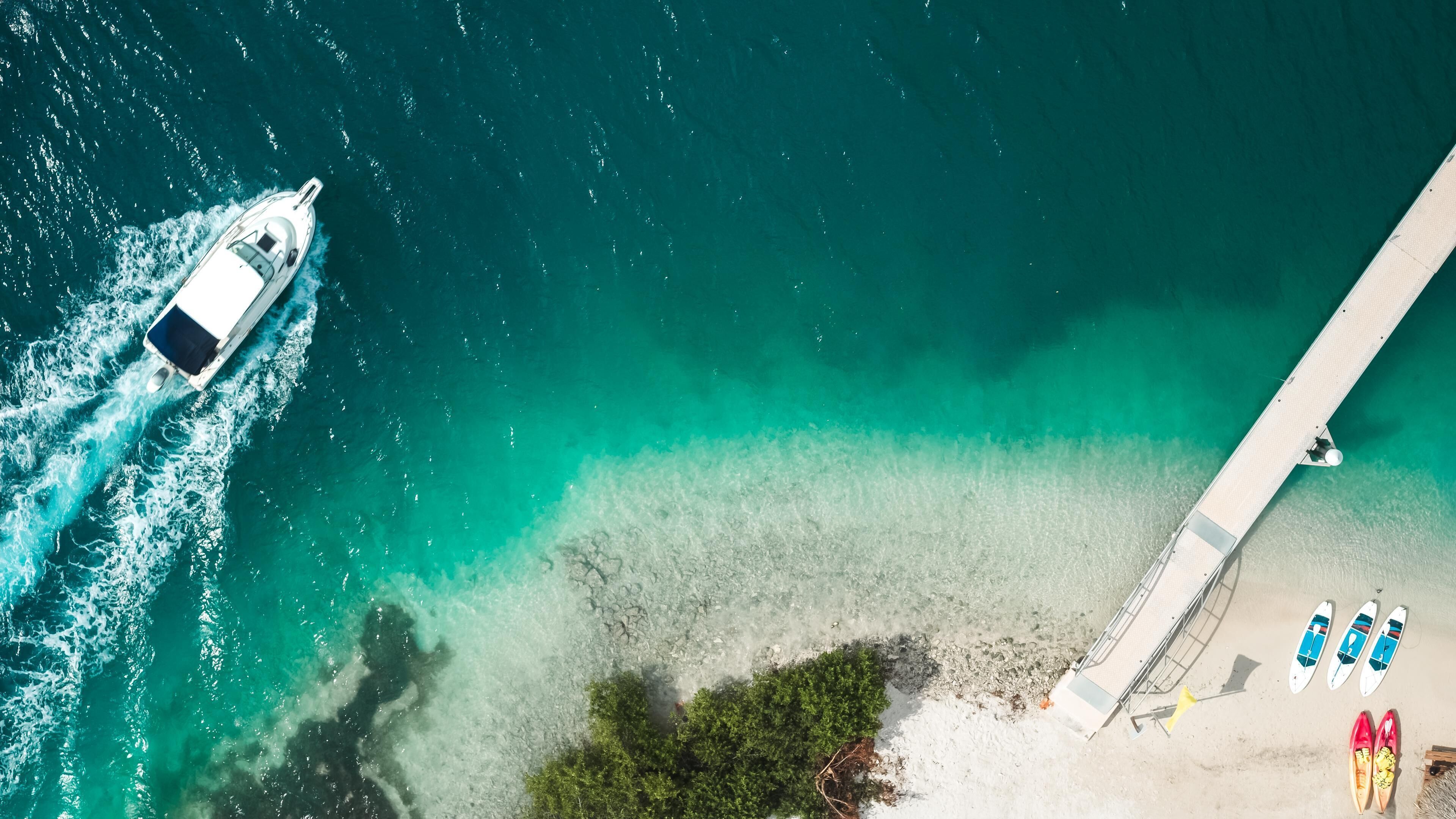 Un bateau sur une eau turquoise, une jetée et une plage avec des planches de surf et des chaussures.