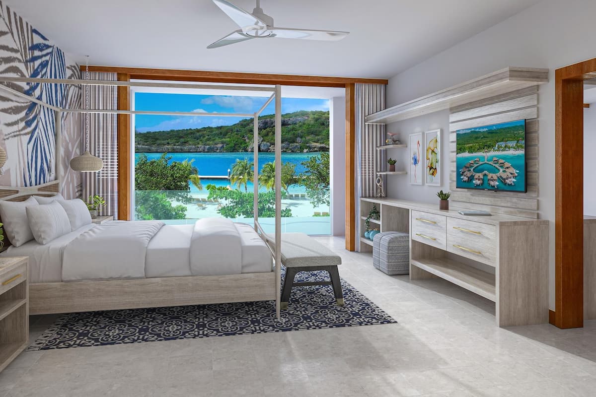 Ein Schlafzimmer mit Bett, Fernseher, Schreibtisch und Blick auf einen Strand.