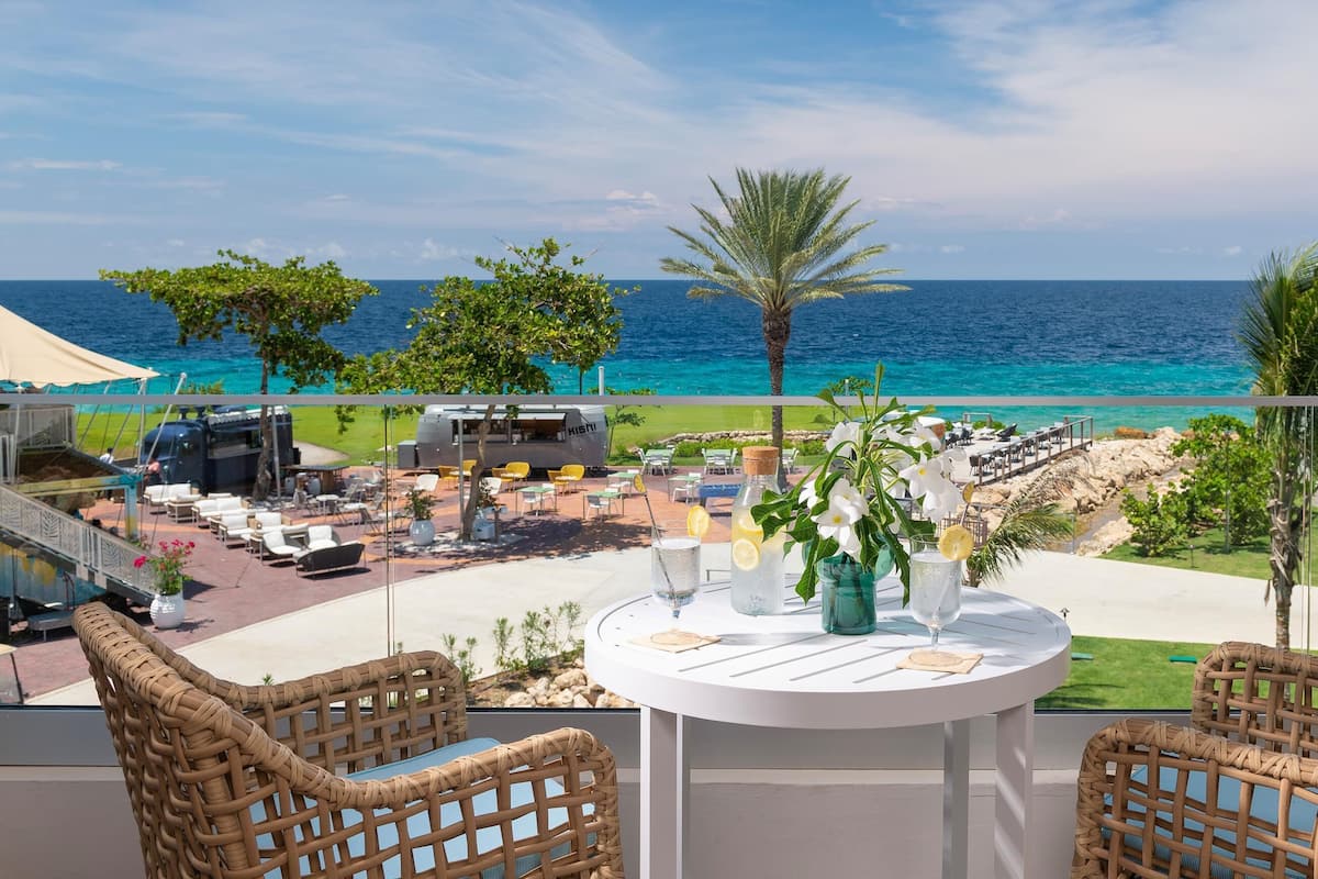 Ein Balkon mit Korbstühlen, einem Tisch mit Getränken und Blick auf das Meer sowie die Annehmlichkeiten des Resorts.