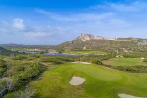 A golf course with bunkers, a flag, and a distant mountain.