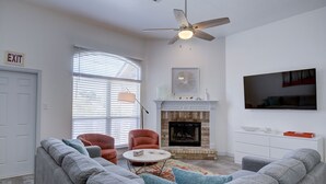 Una sala de estar con chimenea, dos sillones, un sofá, un ventilador de techo y un televisor.