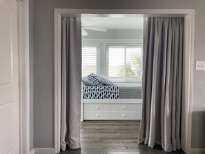 Un dormitorio con una cama, un ventanal con persianas y una puerta con cortinas.