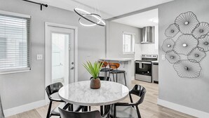 A modern kitchen with a built-in oven, a dining area with a marble table, and a unique wall art piece. - Queens Suite 2BD/2BA Miami Beach Lincoln Casa (Miami Beach)