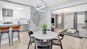 A modern kitchen with white cabinets, a dining area with a marble table, and a living room with a sofa and a TV. - Queens Suite 2BD/2BA Miami Beach Lincoln Casa (Miami Beach)