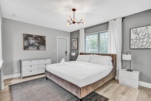 Une chambre à coucher moderne, dotée d’un grand lit, d’une table de chevet, d’une commode et d’œuvres d’art accrochées aux murs.
