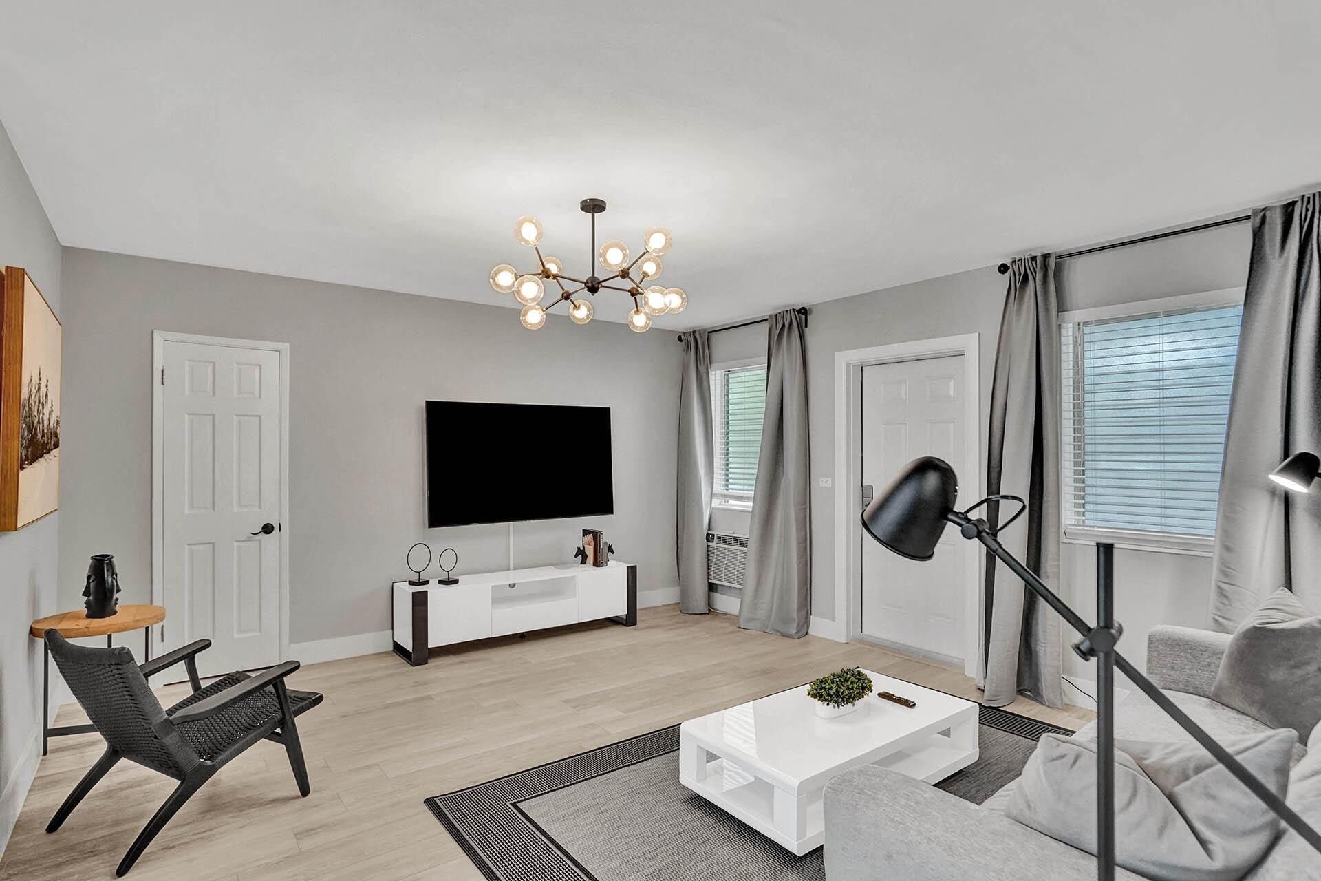 A modern living room with a flat-screen TV, a white entertainment unit, a black chair, a white coffee table, a floor lamp, and a grey sofa.