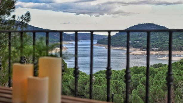 A balcony with a view of a coastal landscape, including a body of water and distant hills.