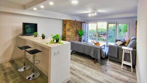 A modern living room with a kitchen area, a stone wall, and a balcony with outdoor furniture.