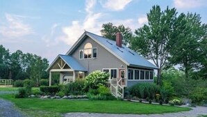 Une maison à deux étages avec un porche couvert, une cheminée et une pelouse bien entretenue.