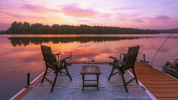 Une jetée en bois avec deux chaises et une table, donnant sur un lac paisible au coucher du soleil.