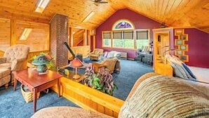 L’intérieur chaleureux d’un chalet avec un plafond en bois, une cheminée, un canapé et une table à manger.