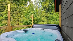 A hot tub on an outdoor deck with a wooden railing and a backdrop of dense green foliage. - Close to Downtown Hot Tub Pet Friendly  (Gatlinburg)