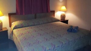 Habitación de hotel con cama, dos lámparas de noche, cabecera y ventana con cortinas.