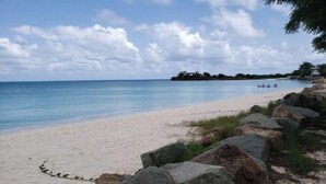 Una playa con rocas grandes al frente y una vista despejada del océano.
