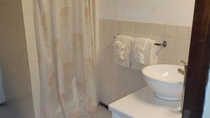 Un baño con cortina de ducha, un lavamanos y dos toallas colgadas en la pared.