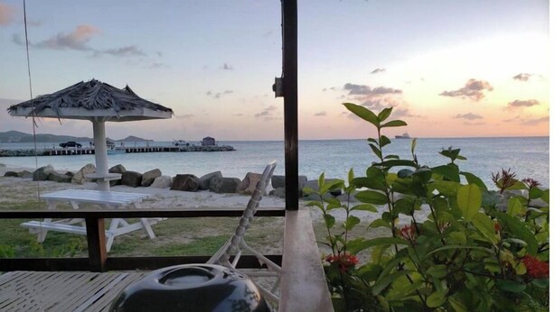 Vista de una playa con una parrilla, sillas de descanso y un quiosco de paja.