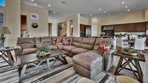 A spacious living room with a sectional sofa, a coffee table, and a dining area with white chairs.