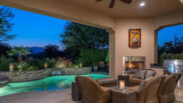 An outdoor patio with a swimming pool, wicker furniture, a fireplace, and a stone wall.