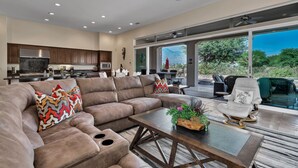 A spacious living area with a large sectional sofa, a coffee table with plants, and a view of the outdoors through large sliding glass doors.