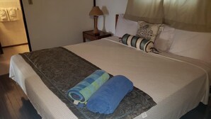 A neatly made bed with a patterned bedspread, two rolled towels, and a bedside lamp.