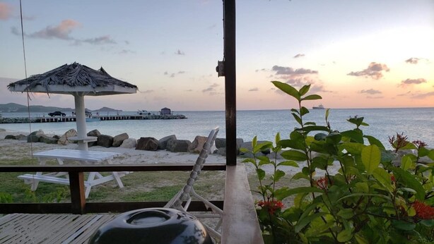 A beach view from a covered deck with a grill and lounge chairs.