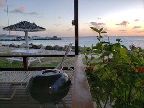 A beach view from a covered deck with a grill and lounge chairs.